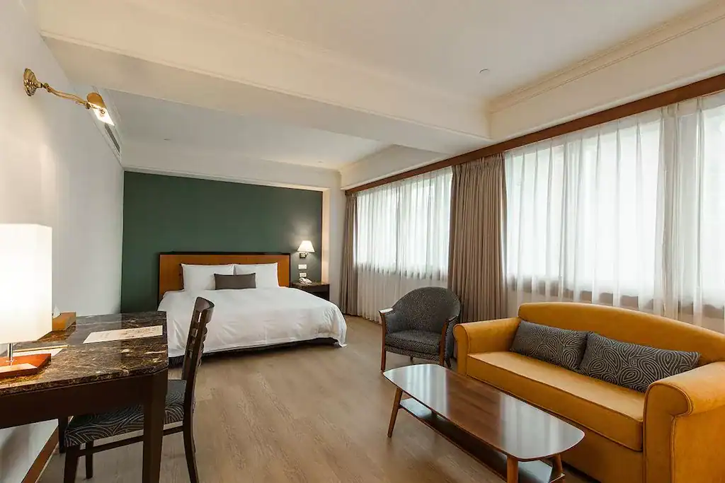 寬敞明亮的雙人客房，配有書桌與沙發區，窗邊採光良好、氛圍溫馨