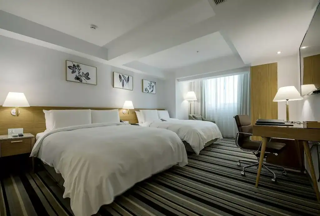 雙人床客房寬敞明亮，搭配書桌與柔光燈飾，營造舒適商旅住宿氛圍
