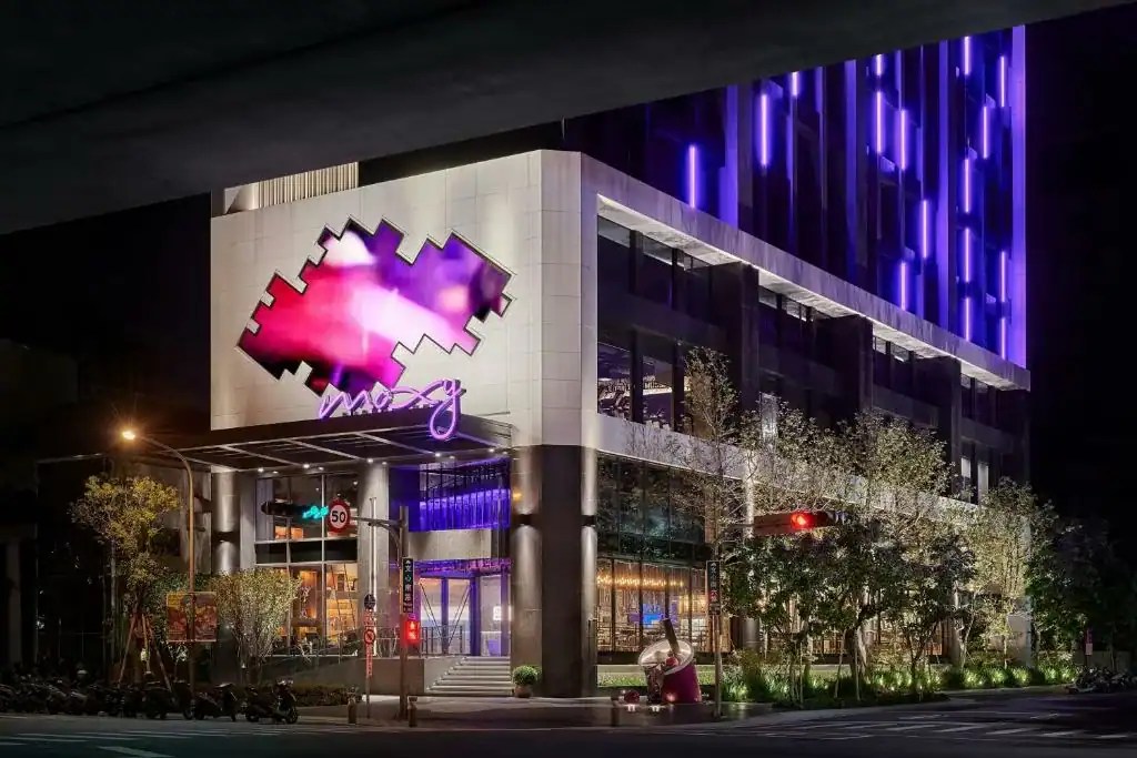台中Moxy酒店夜景外觀，霓虹紫光點綴現代建築，展現潮流設計與都會時尚氛圍
