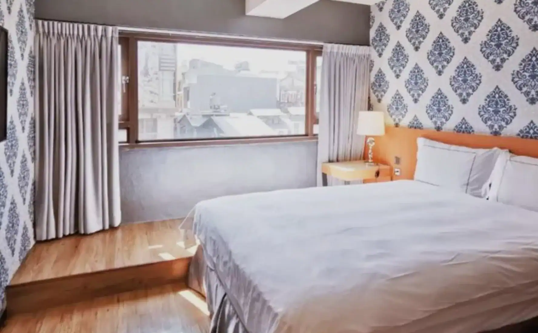 房間擁有大片窗戶與自然採光，典雅壁紙搭配木質地板，呈現現代又溫馨的住宿氛圍。